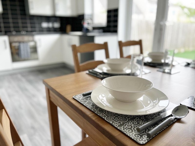 Modern dining table set with place settings, wooden chairs, open-plan kitchen visible in background