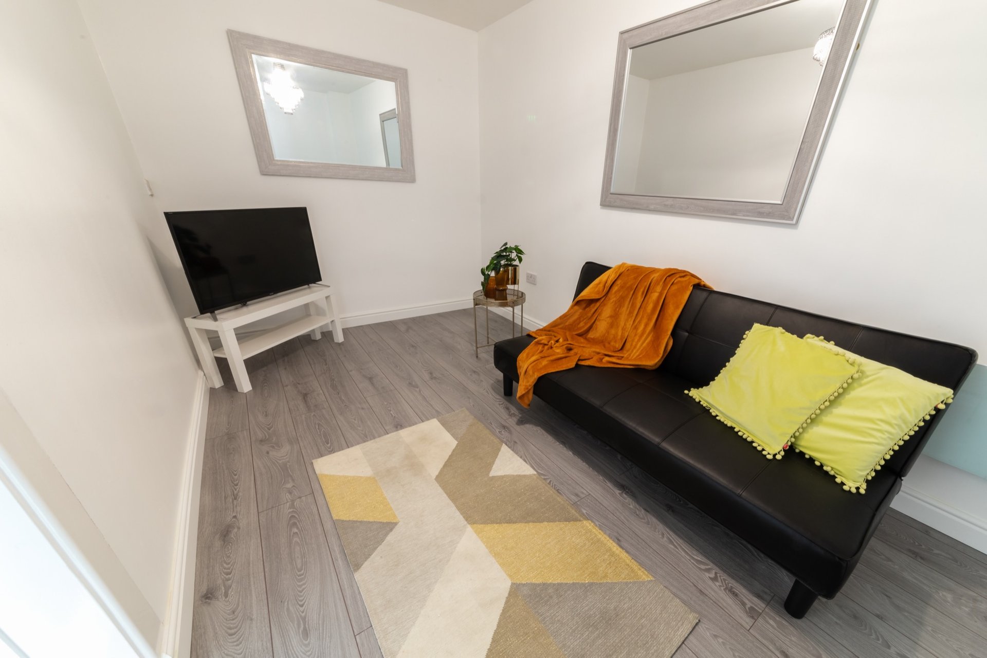 Modern living room with black sofa, geometric rug, TV stand and yellow cushions