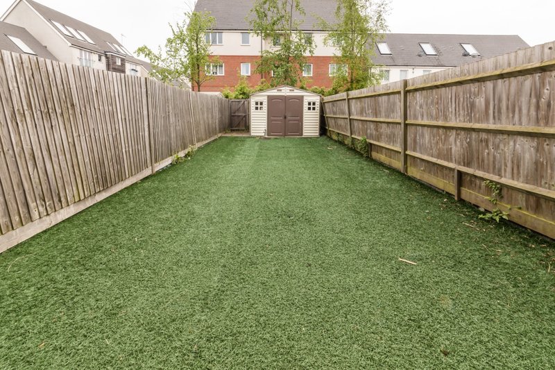 Spacious garden with artificial grass, wooden fencing, and storage sheds