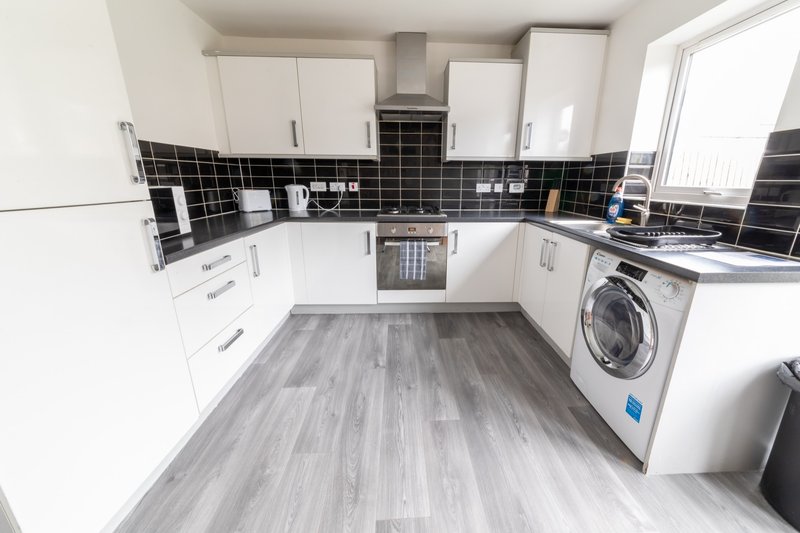 Modern kitchen with white cabinets, black tile backsplash, gray wood-effect flooring, and integrated appliances