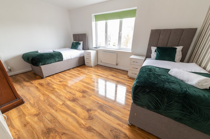 Spacious bedroom with two single beds, wooden flooring, large window and modern furnishings