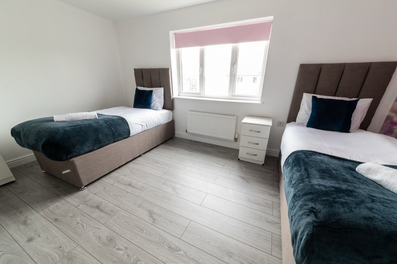 Bright twin bedroom with two single beds, teal blankets, wooden floor and window with pink blind