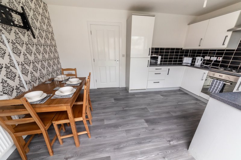 Modern kitchen and dining area with white cabinetry, wooden table, black tile backsplash and grey flooring