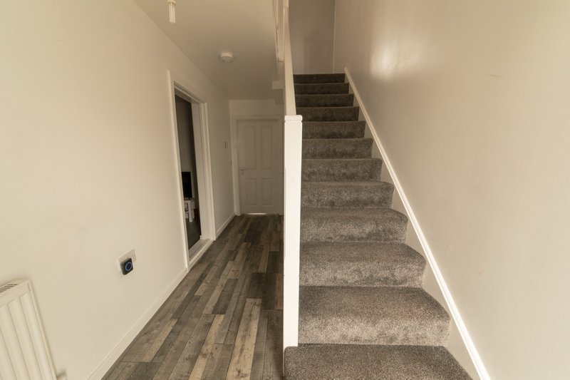 Hallway with wooden flooring, white walls, stairs with gray carpet, and white railing