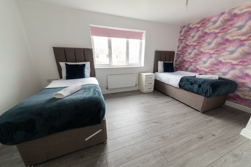 Bright twin bedroom with two single beds, colorful accent wall, wooden flooring and window