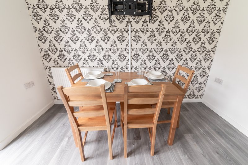 Dining area with wooden table, four chairs, and damask wallpaper