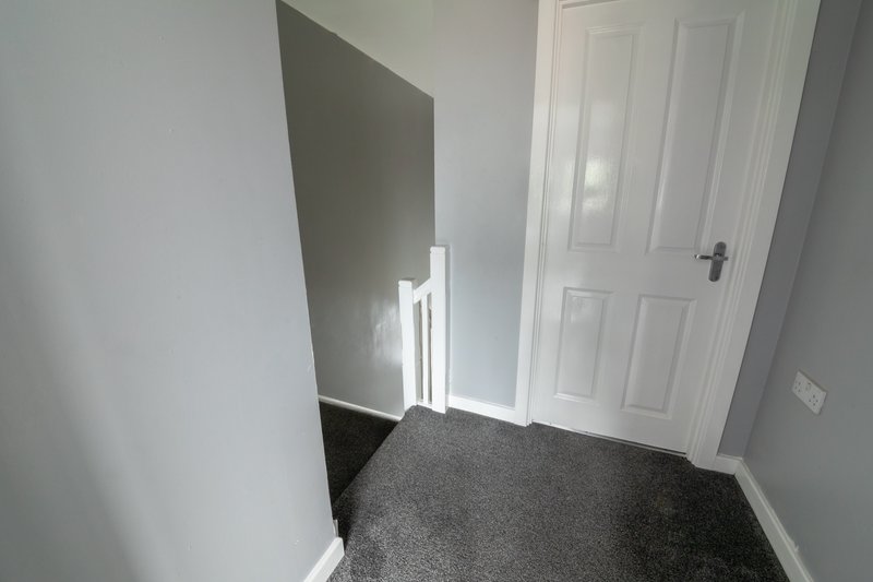 Hallway with white walls, grey carpet, and white panelled door