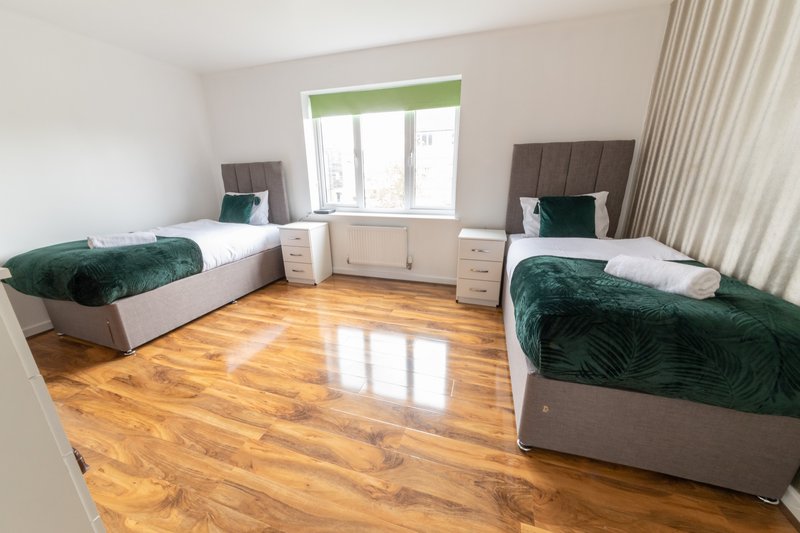 Bright shared bedroom with two single beds, wooden floor, and window with green blind