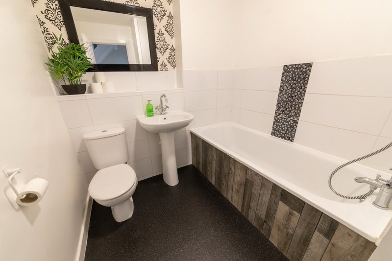 Modern bathroom with toilet, pedestal sink, bathtub, mirror and dark floor tiles