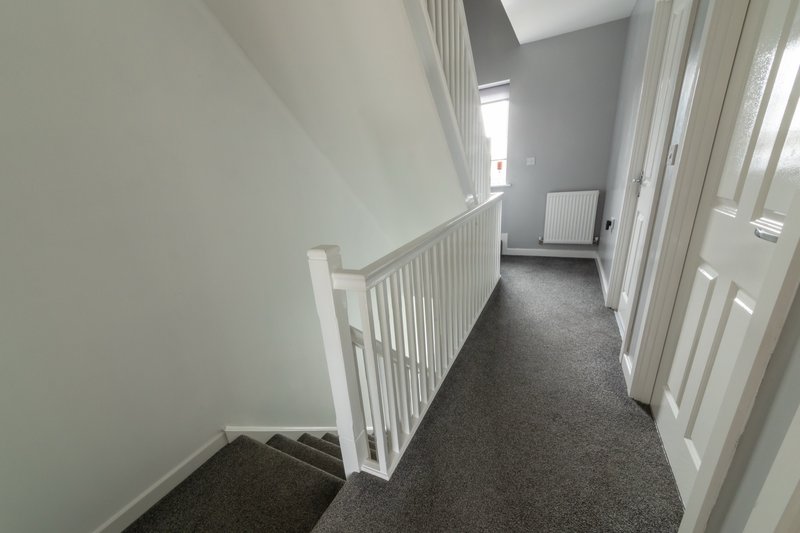 Upstairs landing with white railings, grey carpet, and doors to adjacent rooms