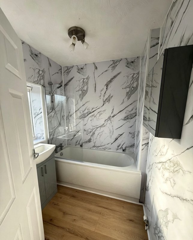 Bathroom with marble-effect wall panels, white bathtub, wooden floor and window