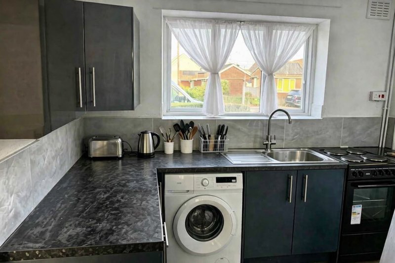 Modern kitchen with dark countertops, washing machine, sink, and window overlooking garden