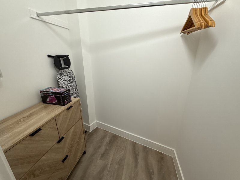 Bedroom corner with wooden dresser, clothing rail, hangers, and vinyl flooring