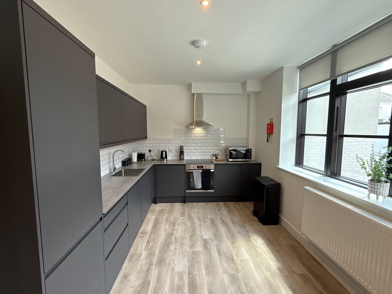 Modern kitchen with dark cabinetry, white subway tile backsplash, wooden floor and windows