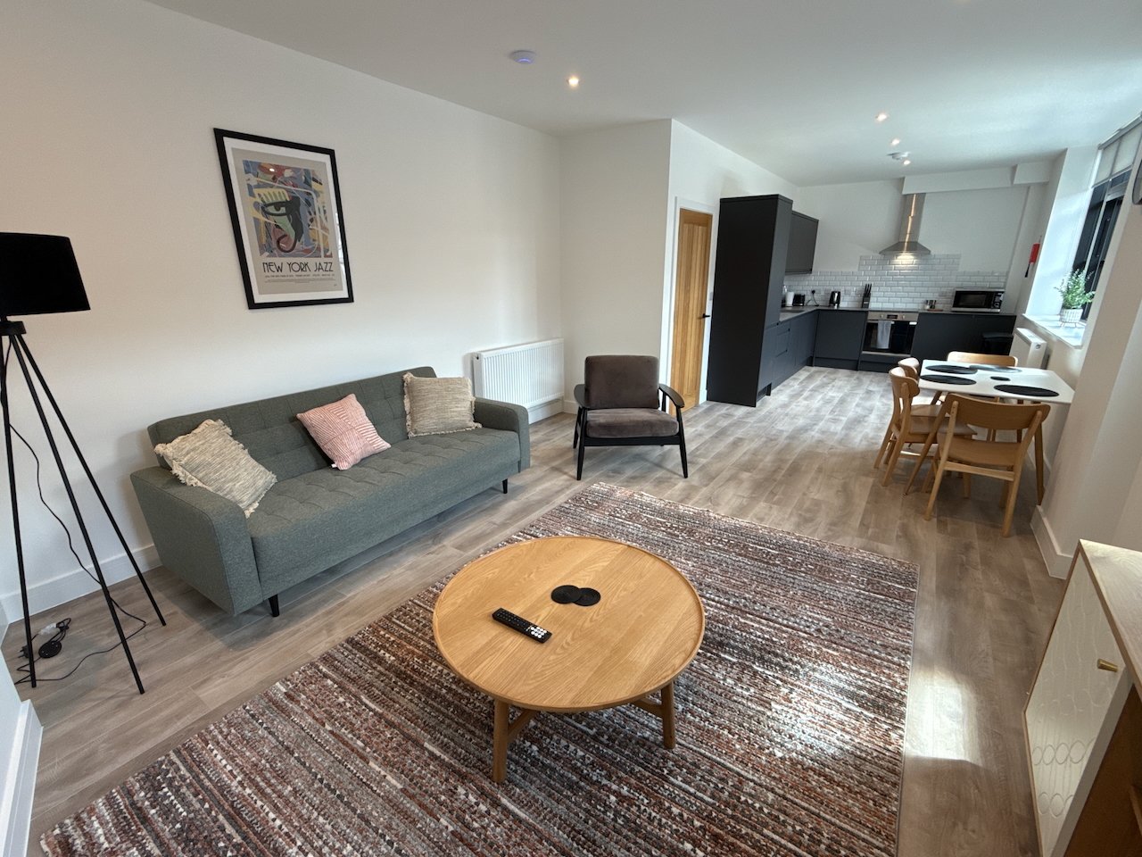 Open-plan living space with gray sofa, wooden coffee table, dining area and kitchen visible