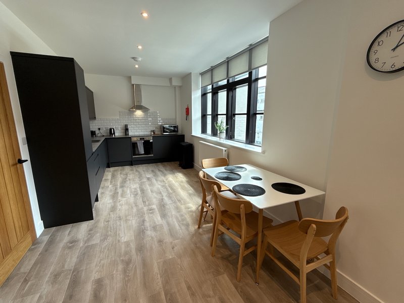 Open-plan kitchen and dining area with wooden dining table, chairs, and modern black kitchen units