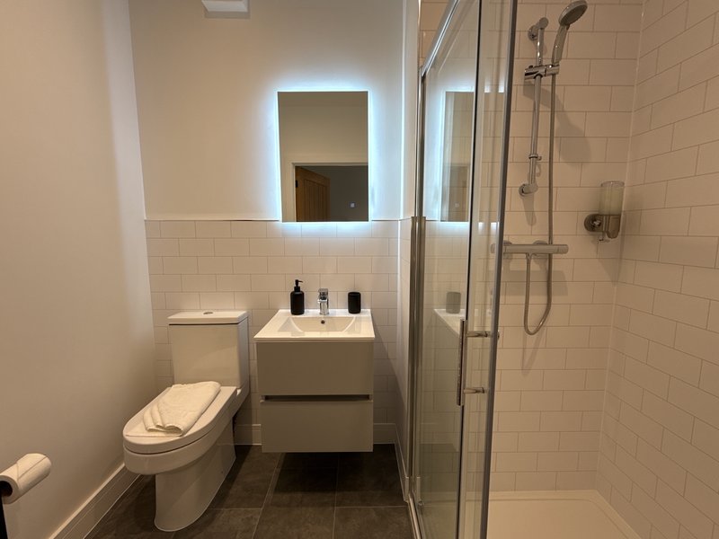 Modern bathroom with illuminated mirror, white sink vanity, toilet, and glass shower enclosure