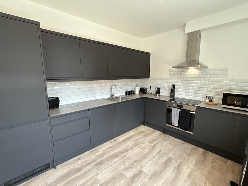 Modern kitchen with dark gray cabinetry, white subway tile backsplash, stainless steel appliances and wooden flooring