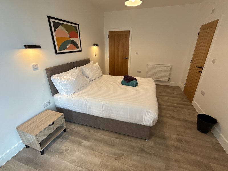 Spacious bedroom with double bed, wooden flooring, wall art, and bedside lighting
