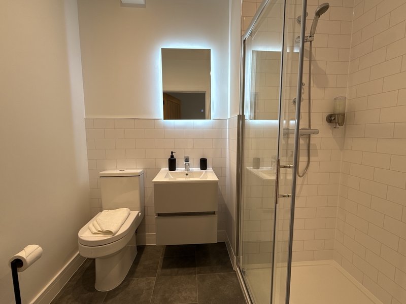 Modern bathroom with toilet, sink, illuminated mirror, shower enclosure and tiled walls