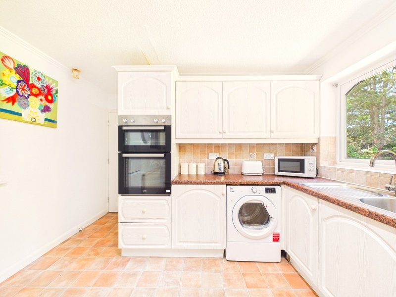 Bright kitchen with white cabinetry, double oven, washing machine, and terracotta floor tiles