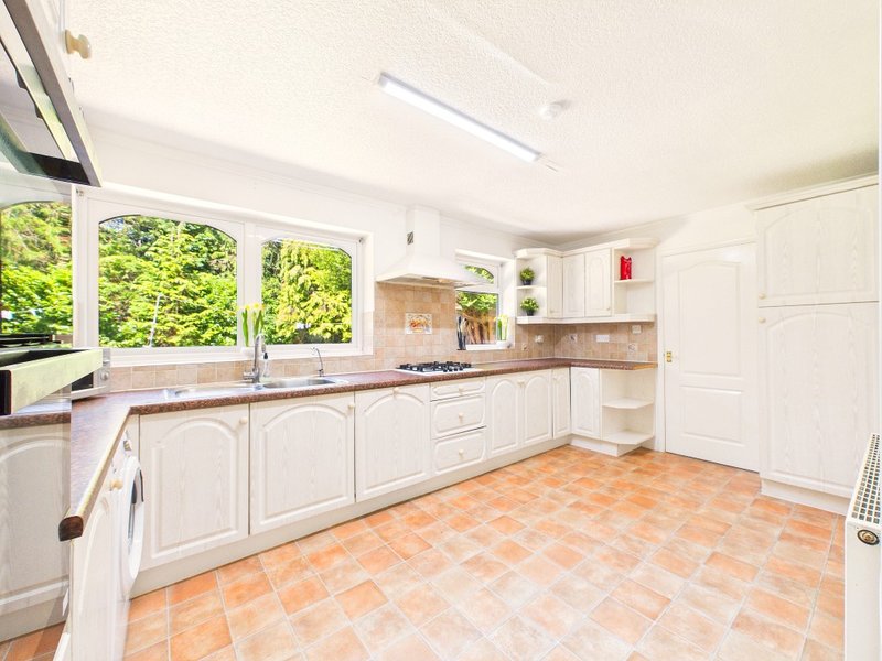 Spacious kitchen with white cabinetry, terracotta tile floor, and garden view through windows