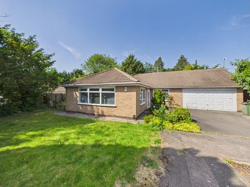 Brick bungalow with driveway, garage, manicured lawn and green surroundings