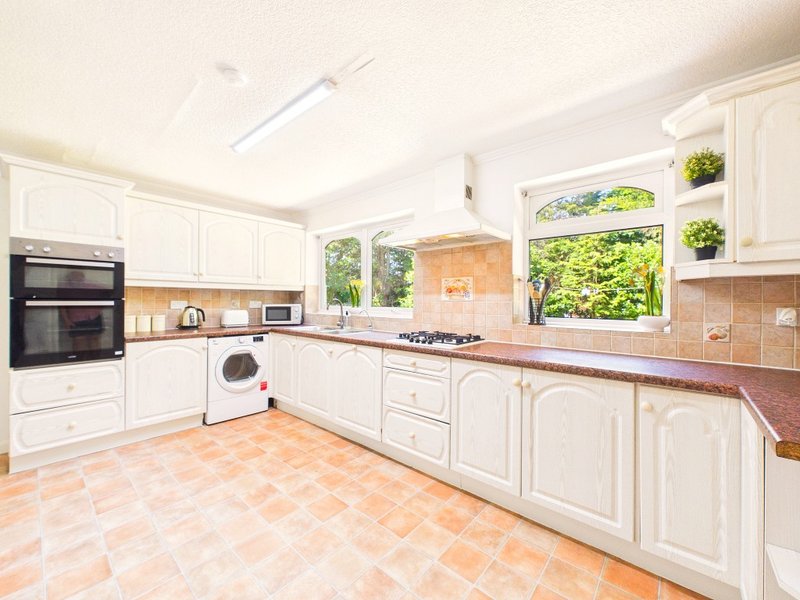 Spacious kitchen with white cabinetry, terracotta tile floor, and garden views through windows