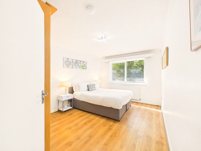 Bright bedroom with double bed, wooden floor, window and yellow door frame
