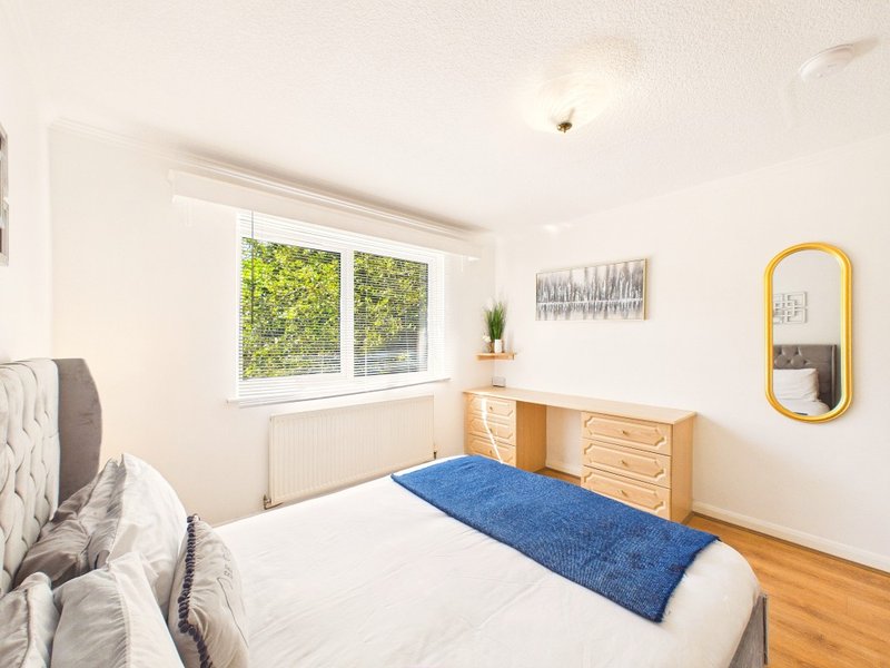 Bright bedroom with double bed, wooden dresser, yellow mirror and window overlooking greenery
