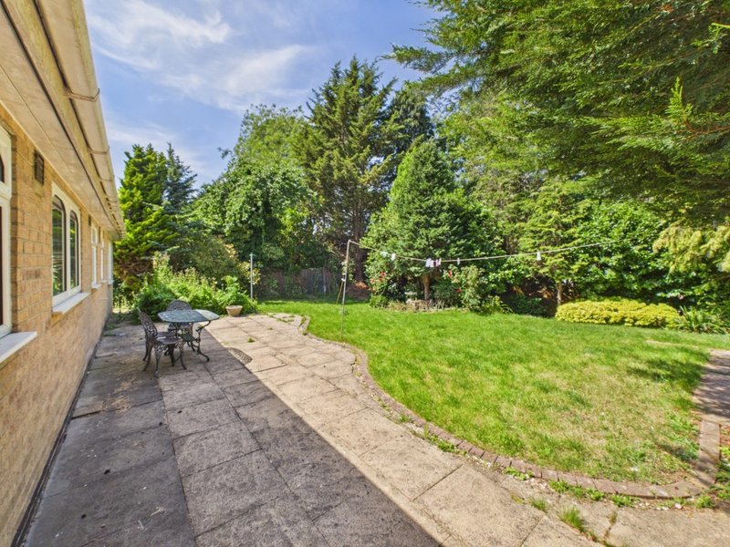 Rear garden patio with seating area, lawn, and mature trees surrounding property