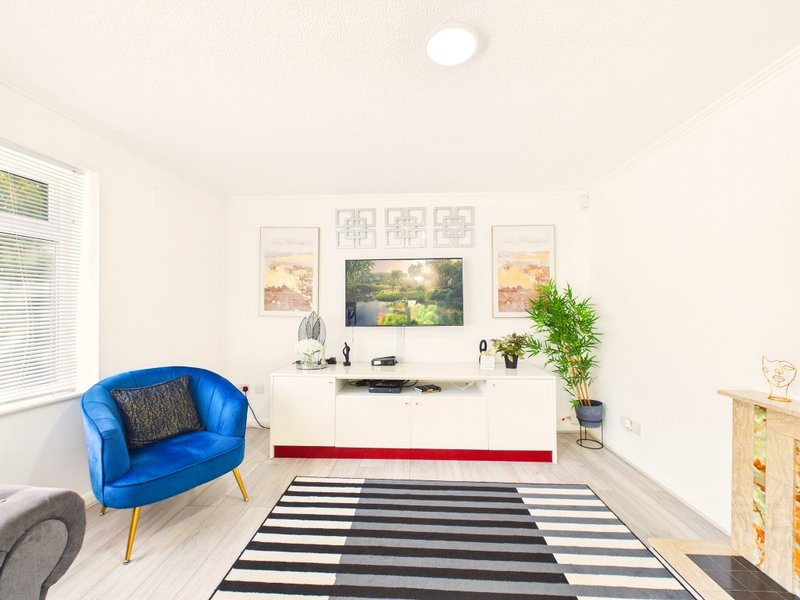 Bright living room with blue armchair, wall-mounted TV, striped rug and potted plant