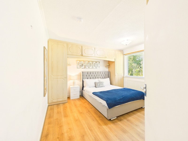 Bright bedroom with double bed, blue blanket, wooden wardrobes and hardwood floor