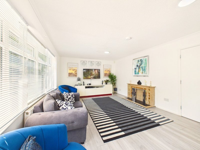 Bright living room with grey sofa, blue armchair, striped rug, wooden storage unit and wall art
