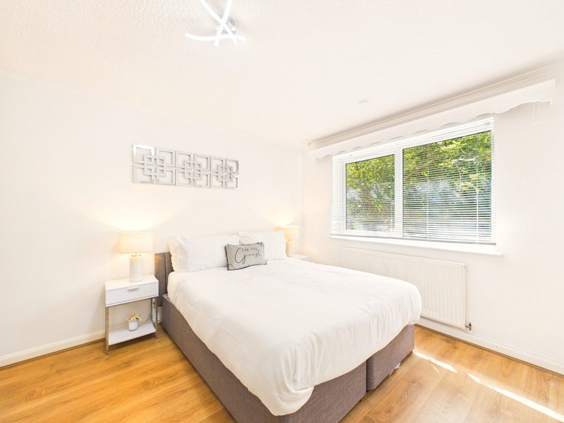 Bright bedroom with double bed, wooden floor, bedside lamps and large window