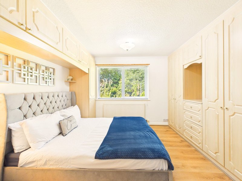 Bright bedroom with double bed, cream headboard, blue throw, cream wardrobes and window