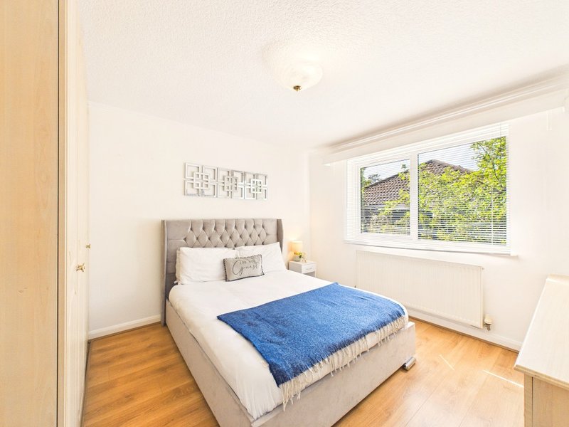 Bright bedroom with double bed, blue throw, wooden floor and large window
