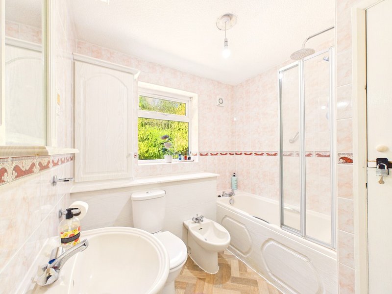 Bright bathroom with white suite, pink tile walls, window with garden view, and shower enclosure