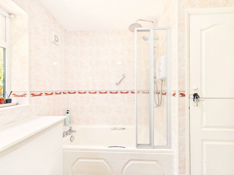 Clean bathroom with white suite, shower enclosure, sink and decorative tile border