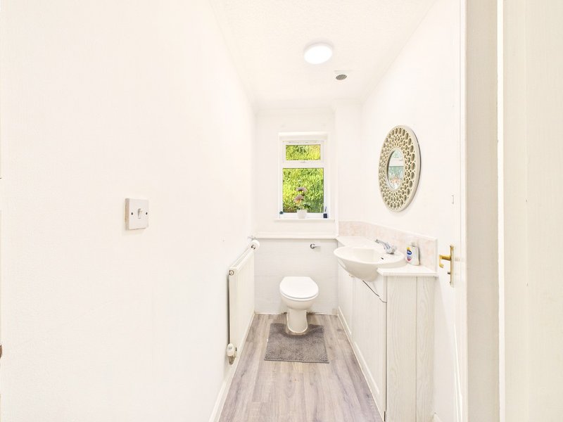 Clean white bathroom with toilet, sink, small window and decorative mirror