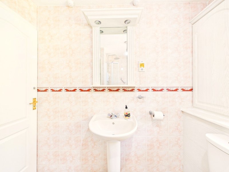 Clean bathroom with pedestal sink, mirror, toilet and decorative tile border