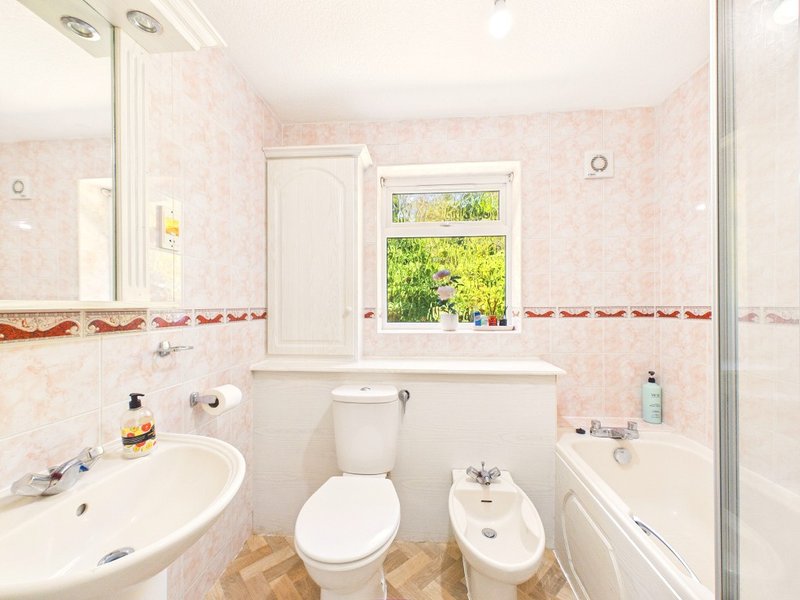 Pink-tiled bathroom with sink, toilet, bidet, bathtub and window overlooking garden
