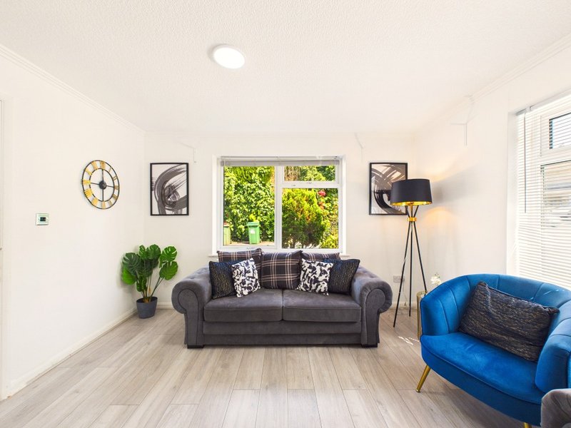 Bright living room with grey sofa, blue armchair, wooden floor and large windows