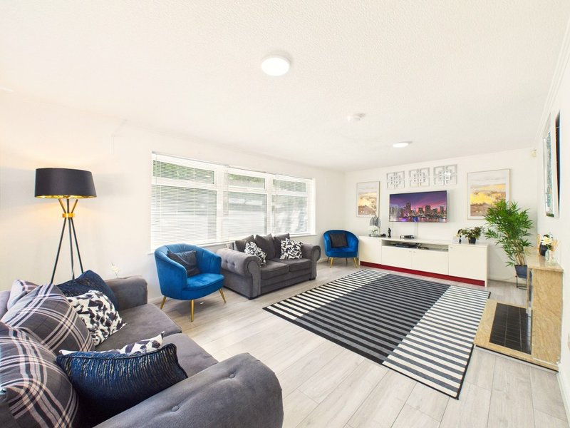 Modern living room with blue armchair, grey sofa, striped rug and wall-mounted TV