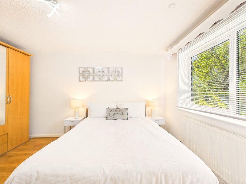 Bright bedroom with double bed, white bedding, wooden wardrobe, and large windows with natural light
