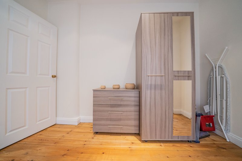 Bedroom with wooden flooring, wardrobe with mirror, chest of drawers, and ironing board
