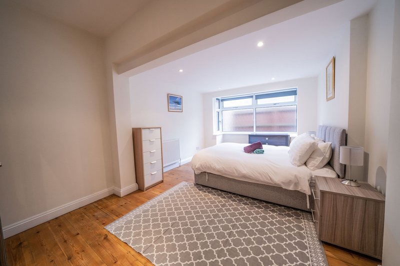 Bright modern bedroom with double bed, wooden flooring, geometric rug and large window