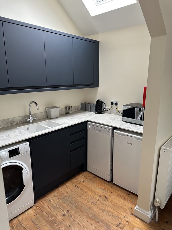 Modern kitchen with black cabinetry, white countertop, washing machine, dishwasher and skylight