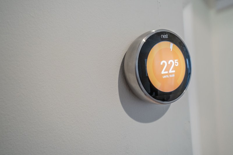 Modern digital thermostat mounted on white wall displaying 22 degrees celsius