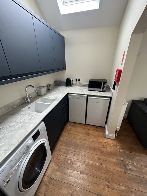 Compact utility room with washing machine, sink, dark cabinetry and wooden flooring